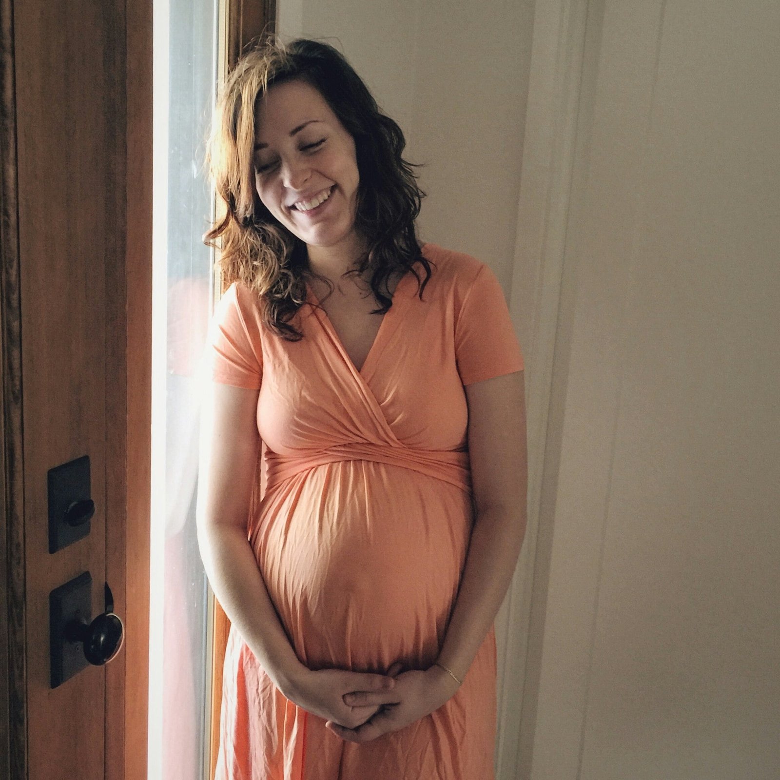 A young woman in her third trimester smiles at the future of holding a precious babe