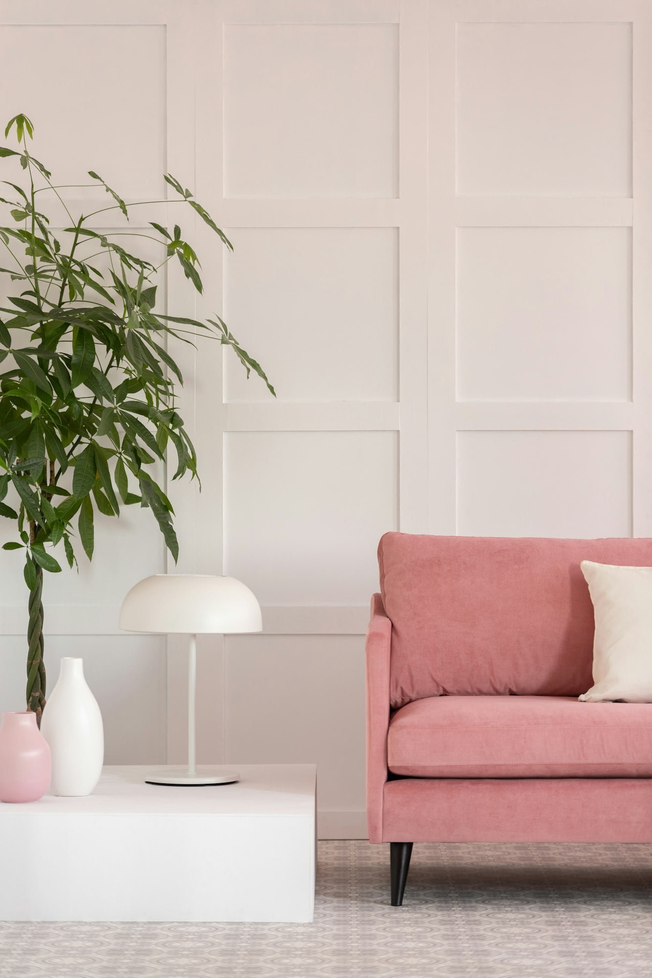 Big green plant in pot next to pastel pink sofa in white elegant interior