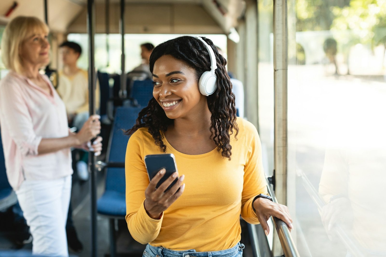 Cheerful black lady using smartphone wearing headphones in bus