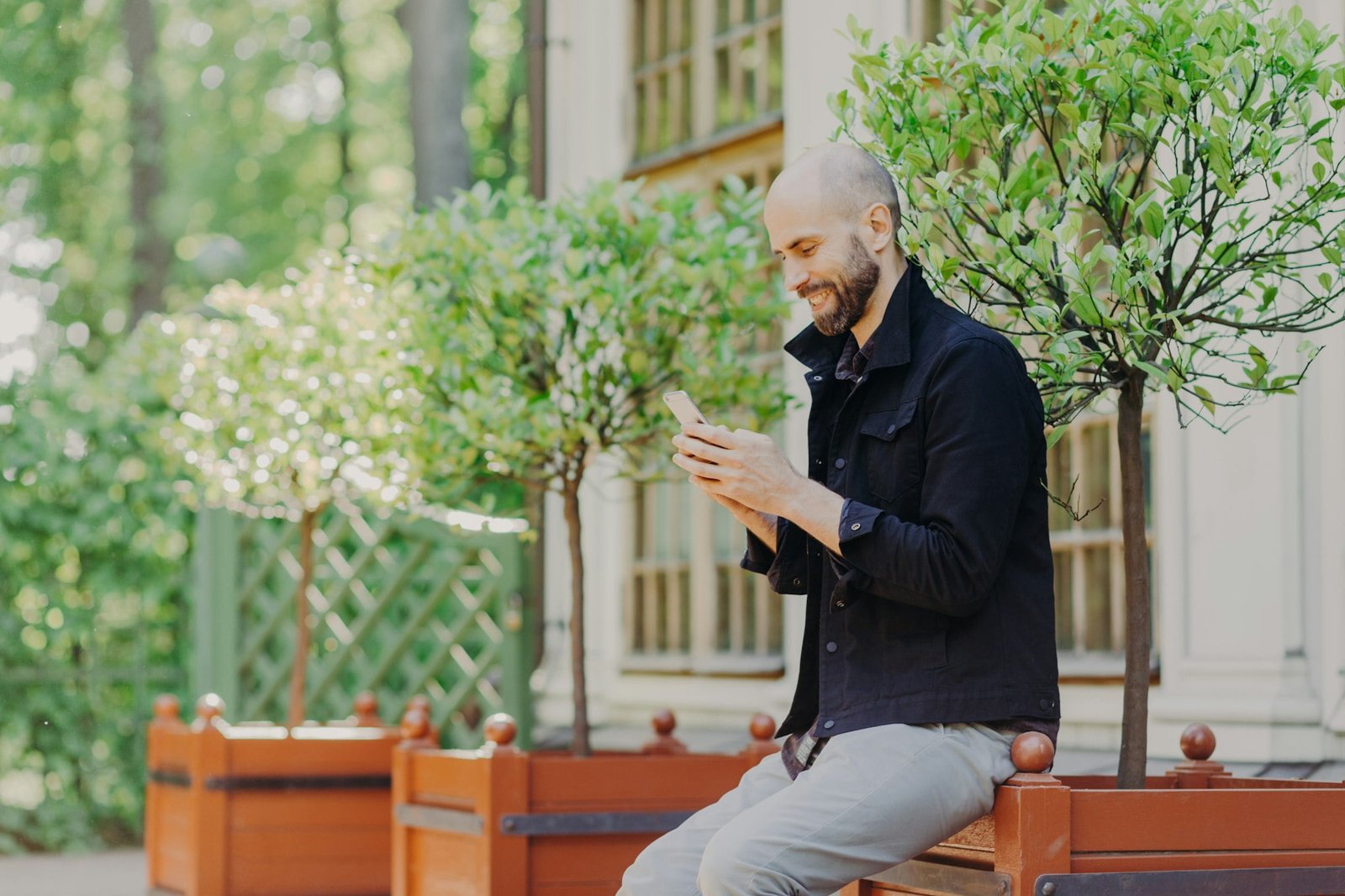 Concentrated male freelancer enjoys day off, breathes fresh air outdoor, uses modern smartphone