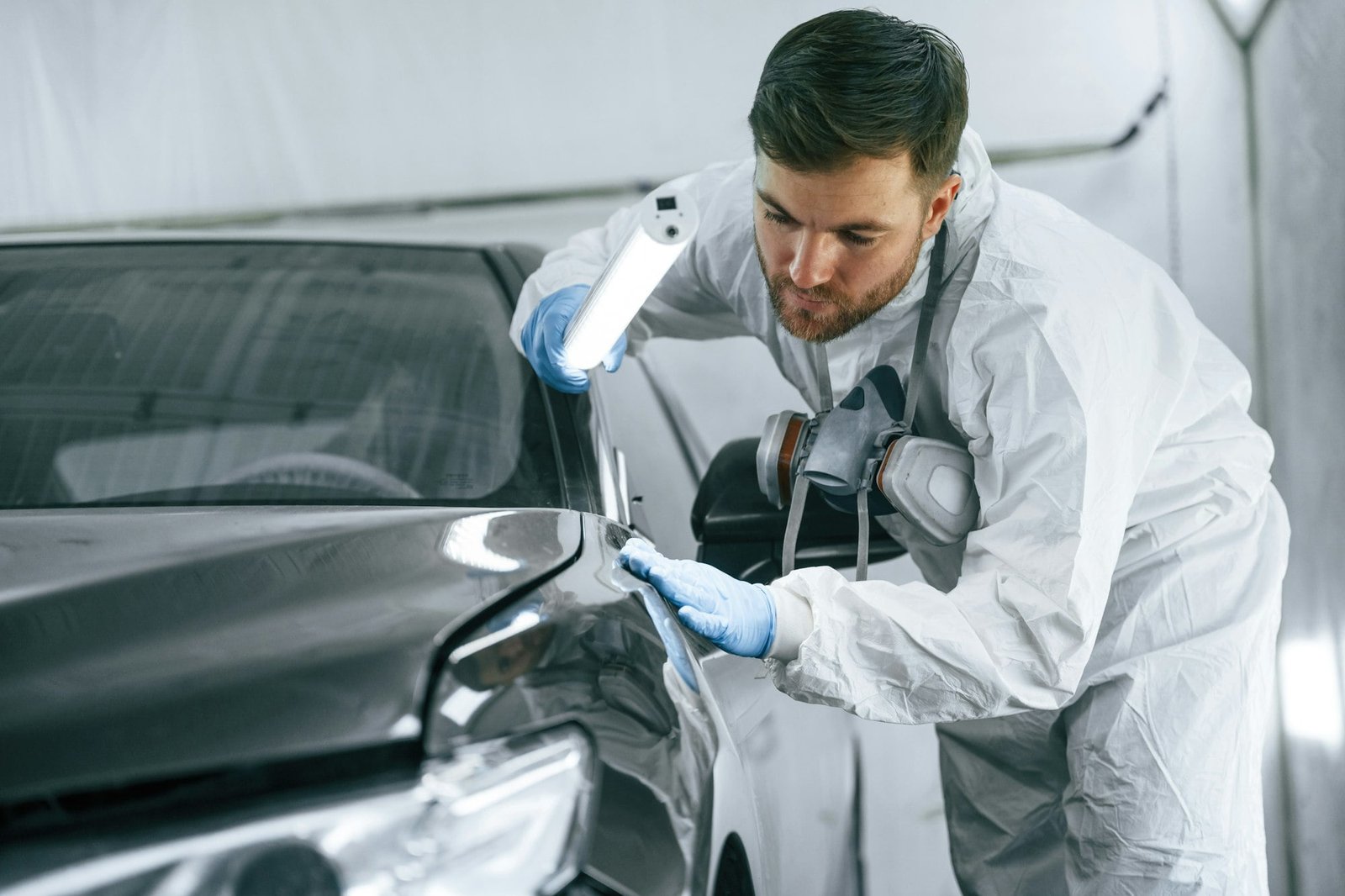 Front part of the automobile. Garage worker is holding lighting and checking surface of the car