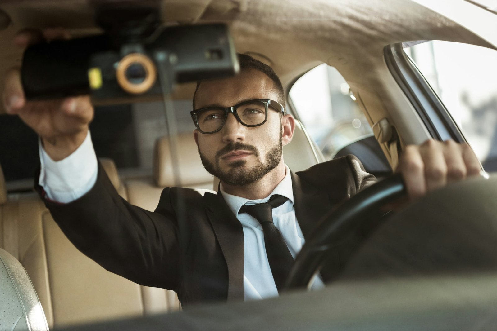 handsome driver in suit driving car and fixing mirror