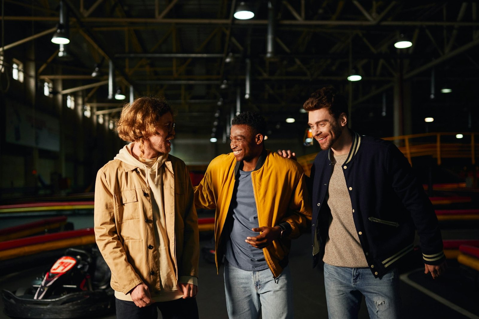 happy diverse friends walking together and chatting inside of karting track, motorsport hobby