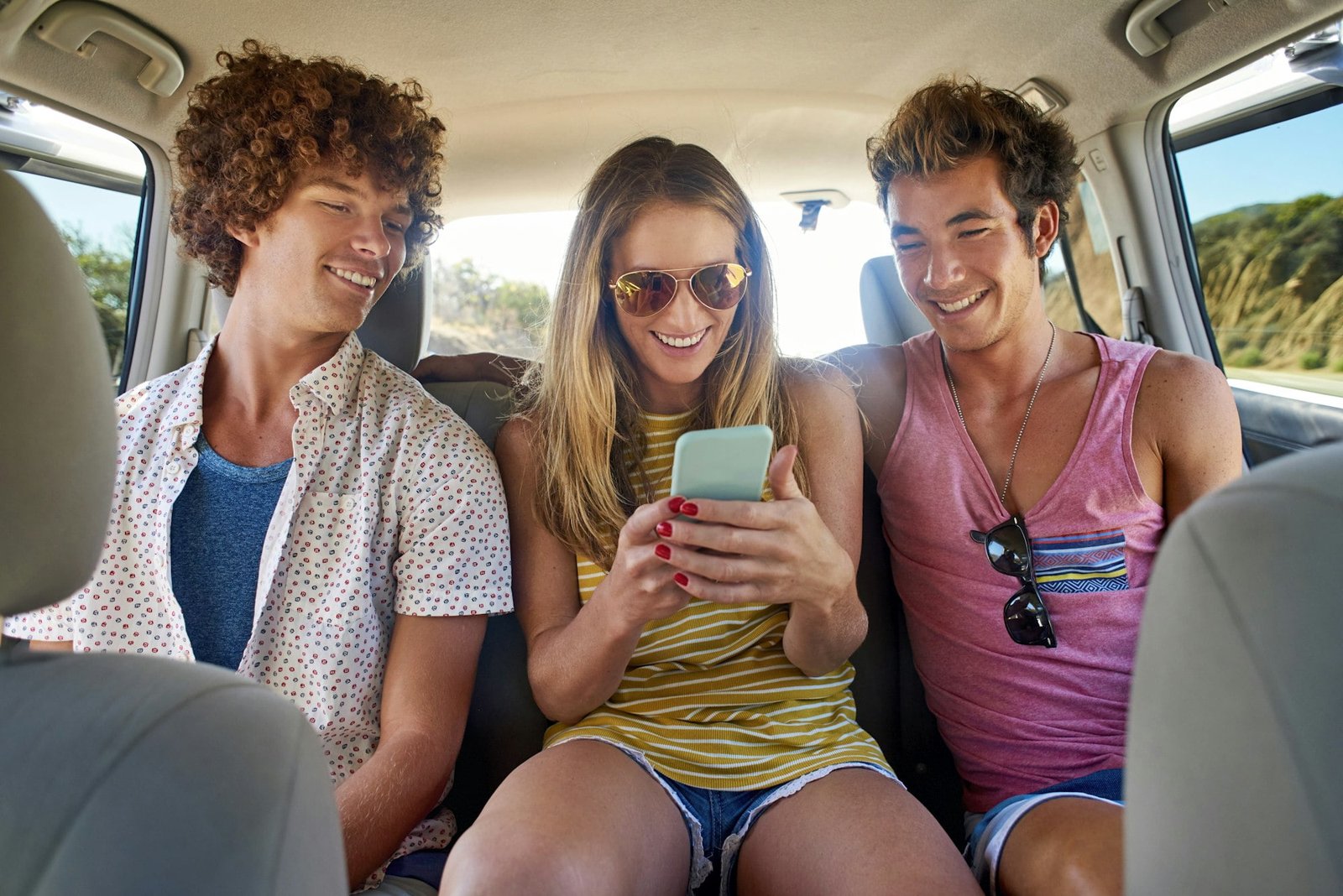 Happy friends checking cell phone in a car