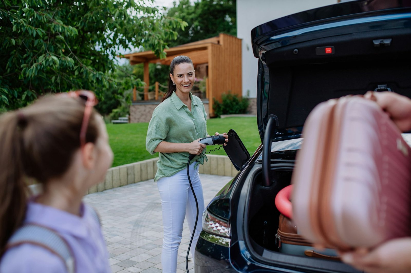 Happy mother holding power supply cable and charging their electric car, rest of family putting