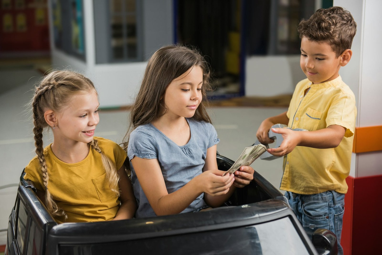 Little girls sitting in toy car at entertainment center.