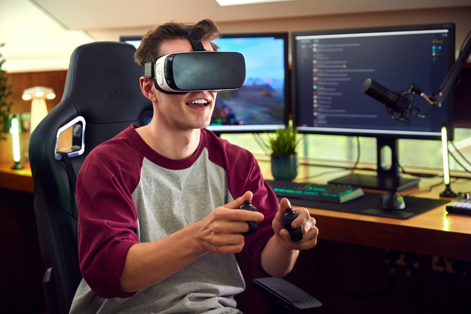 Man Wearing Virtual Reality Headset Gaming At Home Sitting At Desk With Multiple Monitors