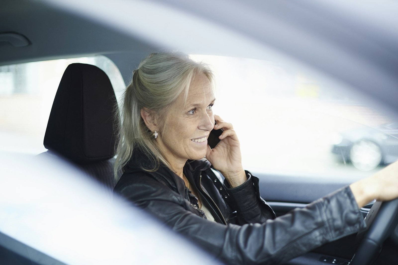 Mature businesswoman chatting on smartphone whilst driving car