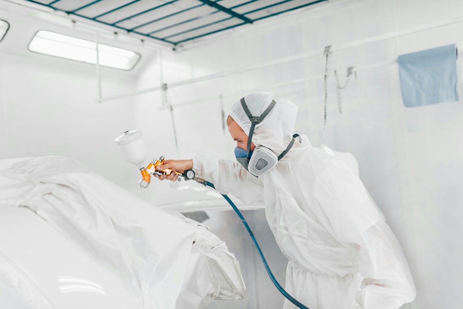 Painter in protective uniform painting car body elements in paint chamber.