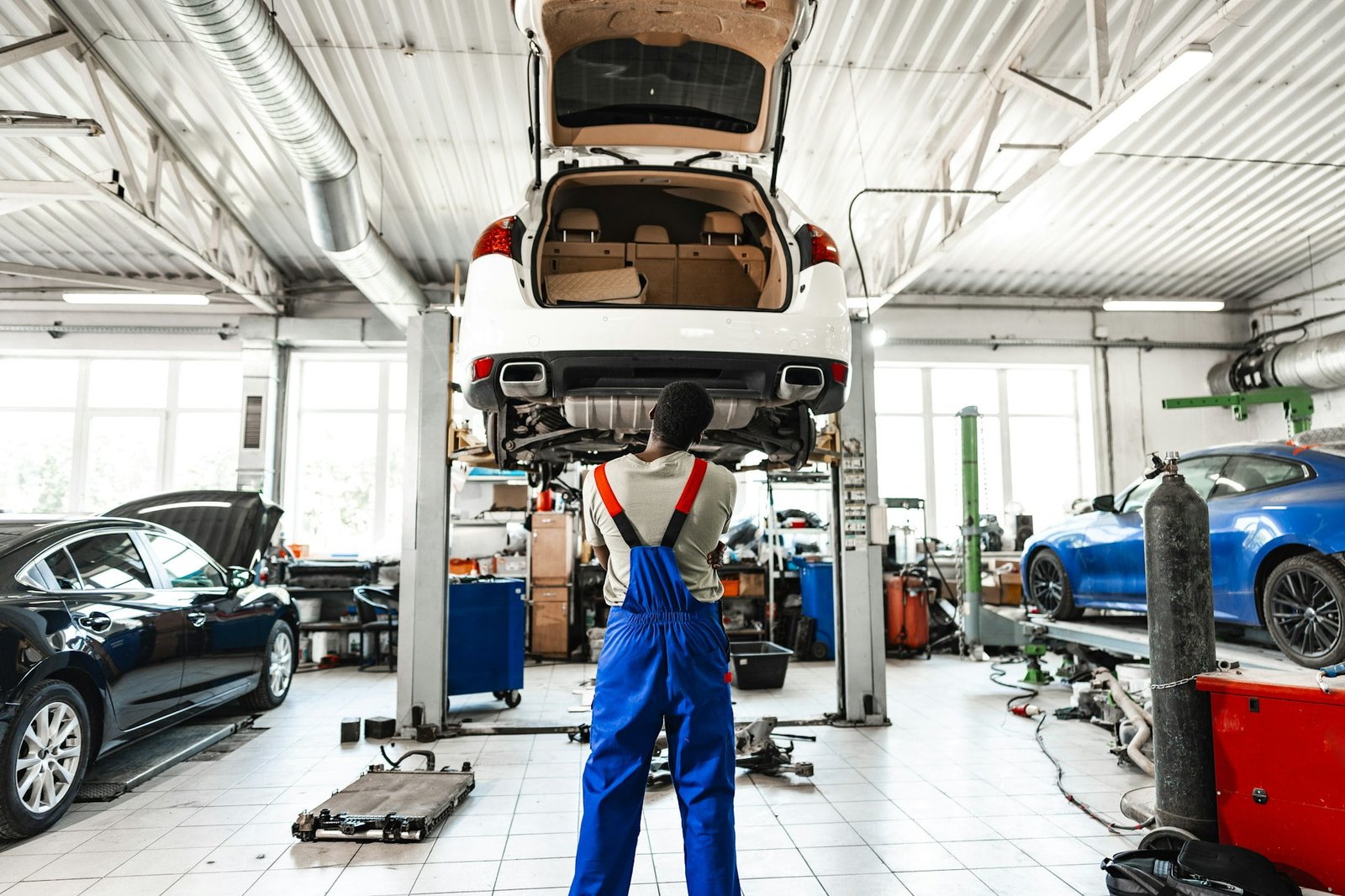 Pensive young African mechanic in car service looking at car thinking of how to repair it