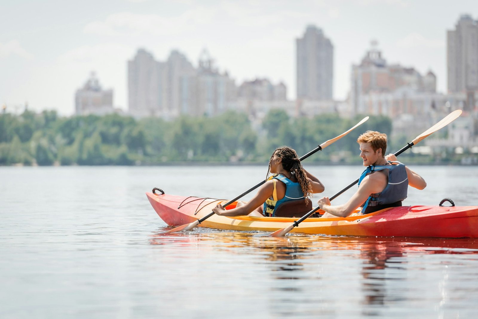 redhead man and african american woman in life vests spending time on river by sailing in sportive