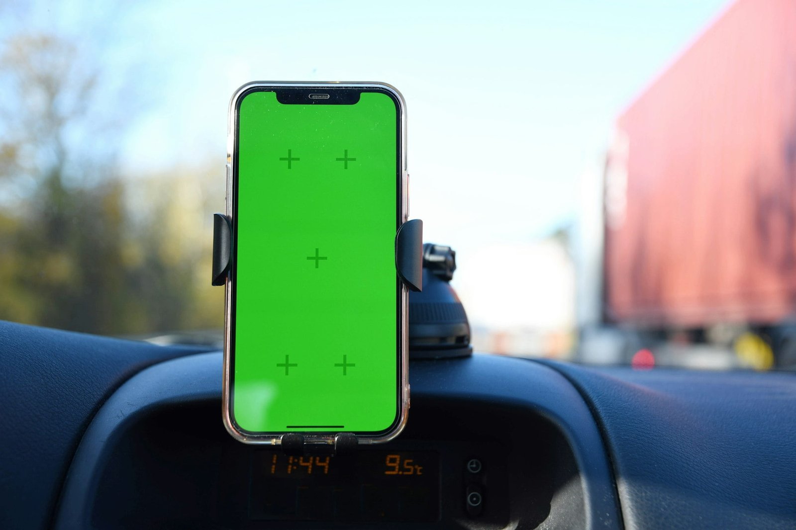 smartphone with green screen on stand in front of windshield in car interior, traffic navigation