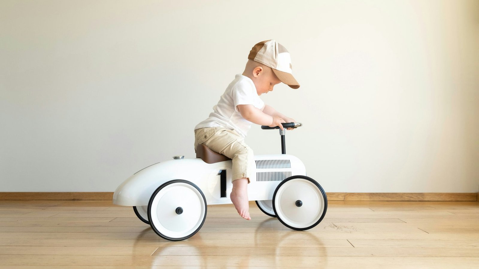 Toddler driving beige retro car. Happy small boy sitting on vintage toy car.