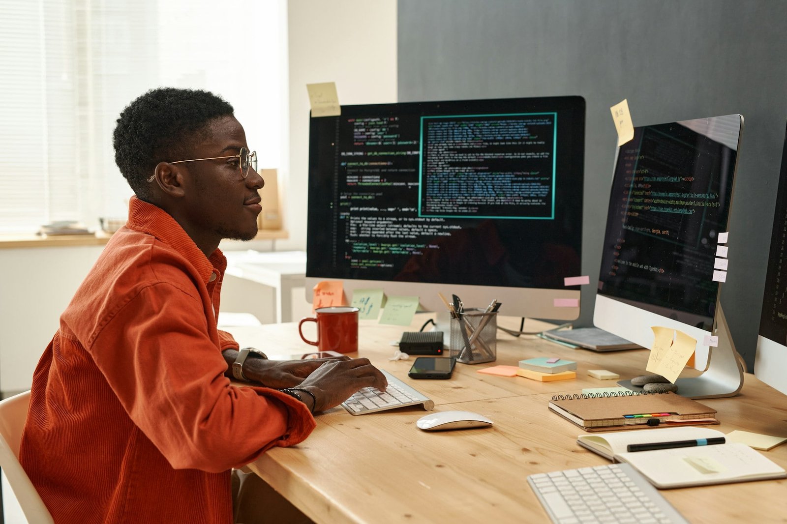 Young serious IT engineer in smart orange shirt looking at coded data